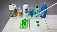 Several multi-surface floor cleaners lined up on a tile surface next to a microfiber floor mop.