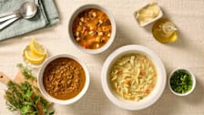 Three bowls of different soups with garnishes and serving utensils.