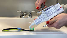 Hands holding toothpaste tube with crank squeezer attached on bathroom sink