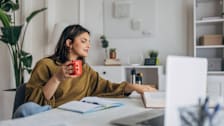 A college student drinking coffee while studying at a desk in a dorm room.