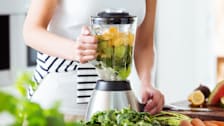 A woman using a blender to make a fruit smoothie in her kitchen.