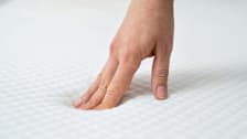 A person using their hand to feel a mattress.