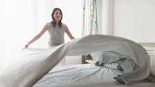 A woman changing sheets on a bed.