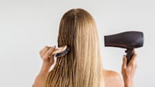 The back of a person's head with comb and hair drying in hands, drying and styling hair.