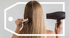 The back of a woman with long blond hair who is holding a brush and a hair dryer.