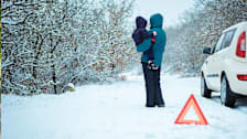 Adult holding a toddler in a snowy landscape next to a parked car and a yield sign.