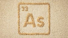Periodic table-style symbol for arsenic  formed from brown rice grains against a background of uncooked white rice