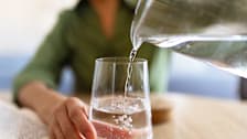 Close up of person pouring water from a pitcher into a glass.