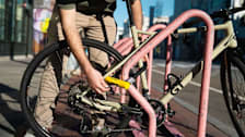 person putting Kryptonite New York FAHGETTABOUDIT Mini U-Lock on bike with city street and buildings in background