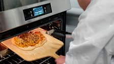 Paul Hope from Consumer Reports taking a cooked pizza out of a Frigidaire oven.