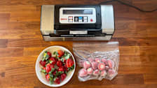 An overhead view of a vacuum sealer with a bowl of strawberries and a bag of vacuum sealed strawberries on a wooden kitchen counter.