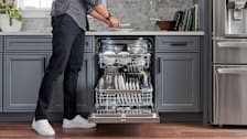 person taking dishes out of dishwasher filled with white dishes in kitchen with grey cabinets