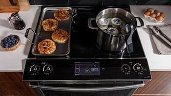 overhead view of GE Profile PHS93XYPFS electric induction range with blueberry pancakes on griddle and pot with water and cans with preserved foods