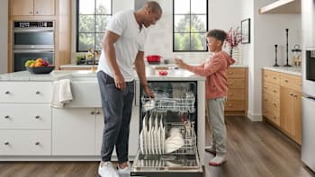 parent and child unloading LG LDFC2423V dishwasher in kitchen with white and wood cabinets