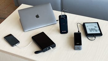 electronic devices on a table being charged by portable chargers: Mophie Powerstation Pro AC 27,000mAh 100W, RAVPower Pioneer AC Portable Charger & Power Bank 20,000mAh and Anker Prime Power Bank 27,650mAh 250W