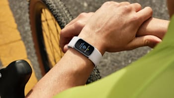 close up of person's wrist with Fitbit Charge 6, bike wheel and asphalt in background