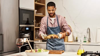 Young Black man taking a chicken cooked in a glass container out of the oven in a home kitchen environment.