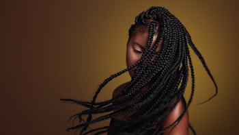 Woman with long, intricately braided hair partially covering her face, against a warm-toned gradient background