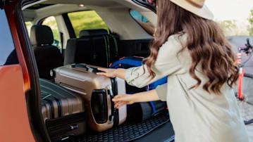 person in beige shirt and hat loading rolling suitcase