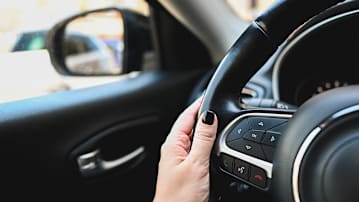 Hand with dark nail polish holding a steering wheel in a car.