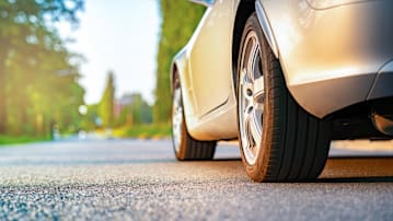low angle of side of grey car on road with blurred tress in background