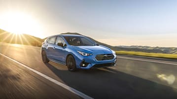 2026 Subaru Impreza driving on a highway with the sun setting behind it.