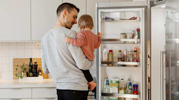 Parent holding a young child next to an open refrigerator.