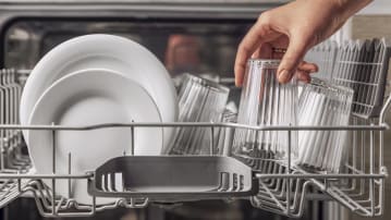 detail of hand taking glass out of dishwasher with glasses and white plates