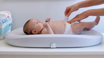 Baby on Hatch Grow Smart Changing Pad, mom adjusting diaper