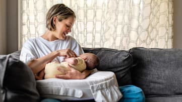 A mom holding her newborn baby on a nursing pillow
