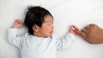 a sleeping newborn baby holding an adult's hand