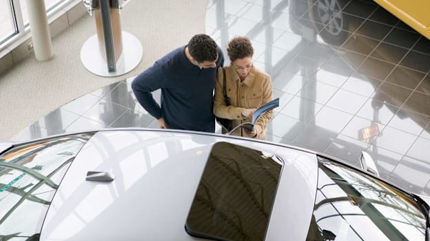 two customers at an auto dealership reviewing details about a new car