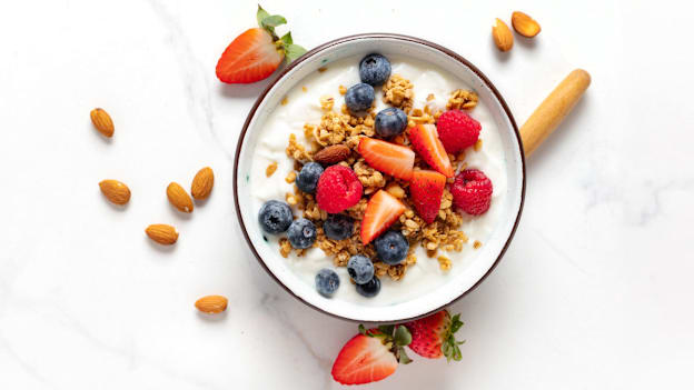 overhead view of bowl of yogurt with granola, almonds, blueberries, raspberries, and strawberry slices