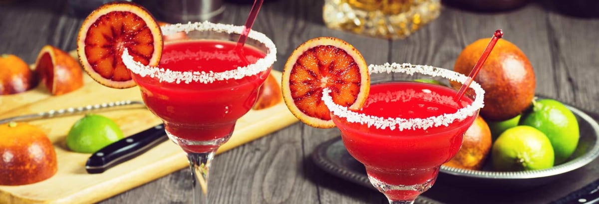 Blood orange margaritas with ingredients on bar.
