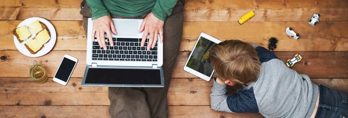Parent browsing on computer while sitting next to child on iPad.
