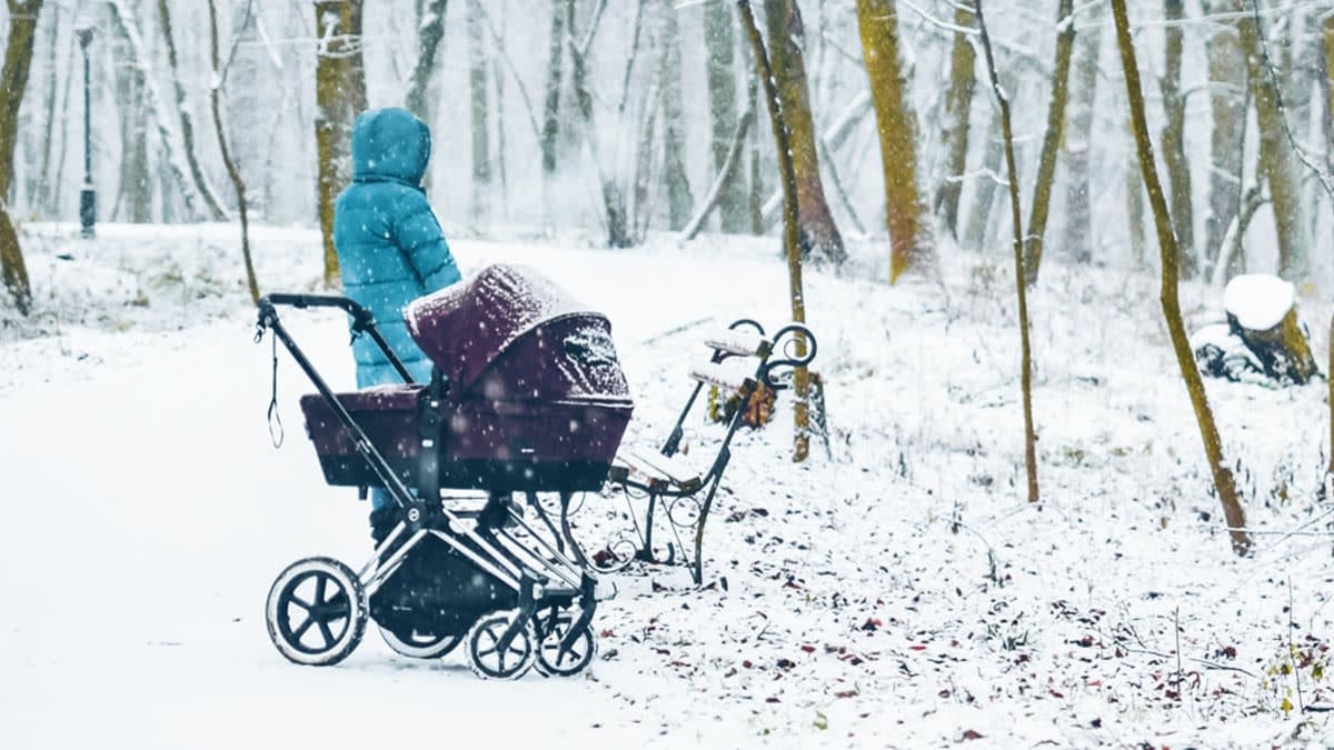 Mother walking with child in baby carriage in winter snowed park