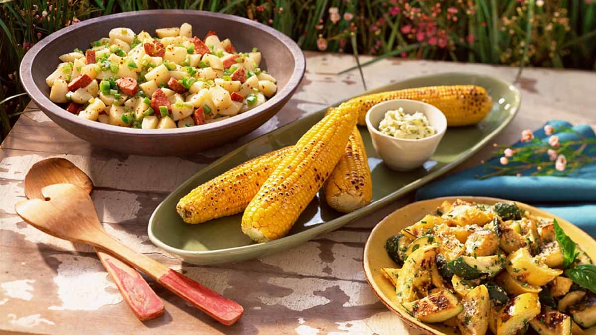 Potato salad, grilled corn on the cobb and zucchini salad on picnic table