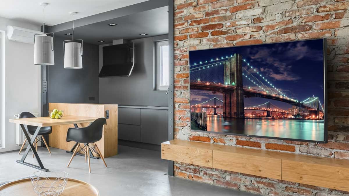 wall mounted TV on brick wall with dining room chairs and table in background