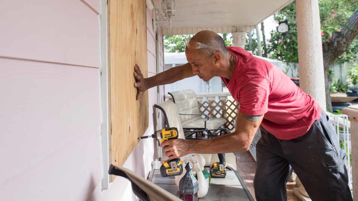 person putting up plywood to protect windows of home
