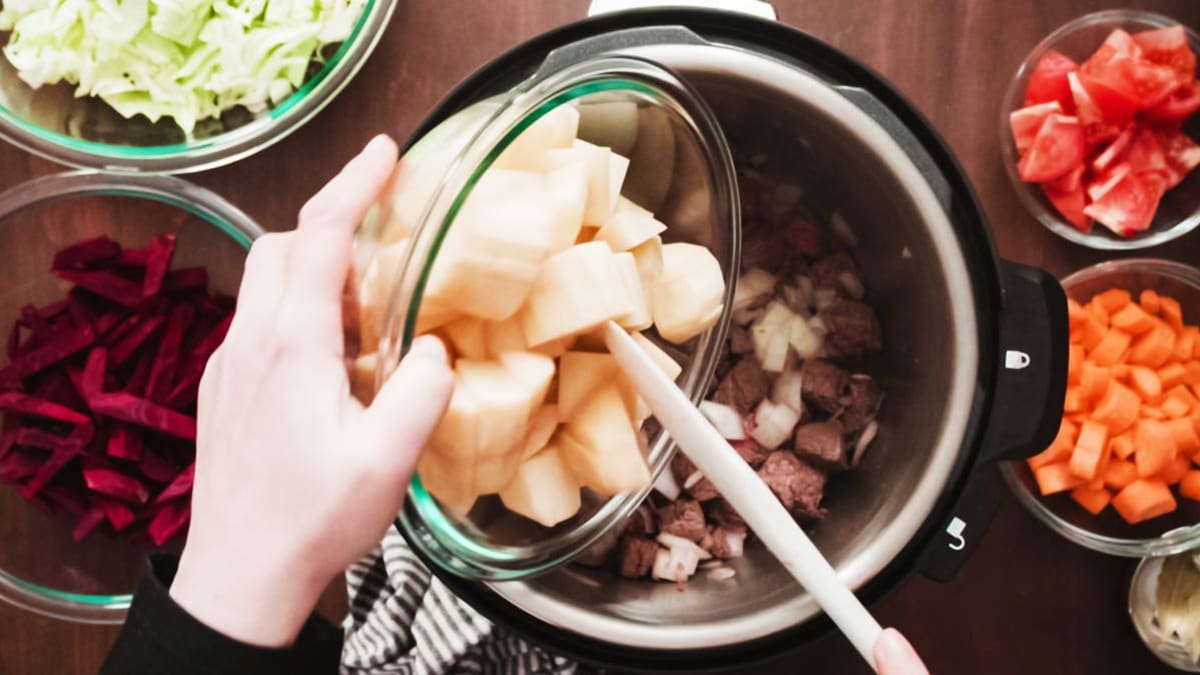 Bowls of chopped vegetables being poured into a slow cooker.