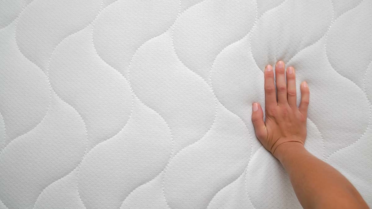 Hand pushing into a soft mattress.