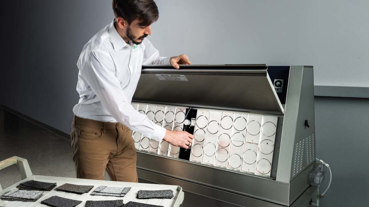 Technician looking at Accelerated Weathering Tester with cart of shingle samples nearby