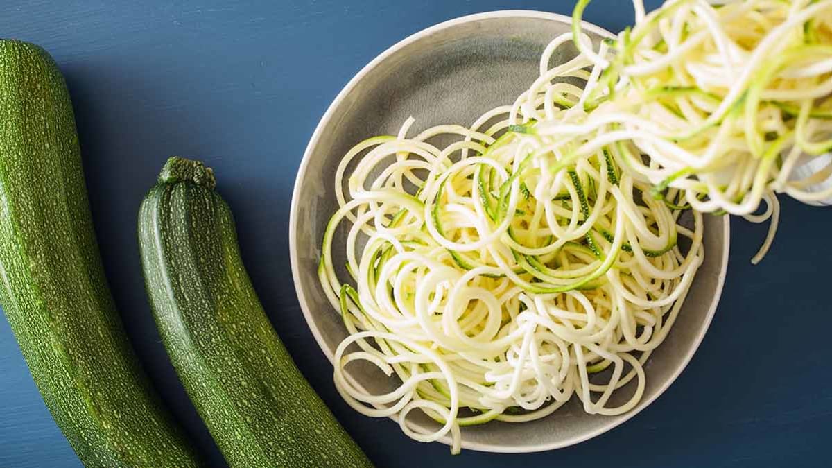 overhead view of zucchini spirals in bowl with 2 zucchini next to bowl