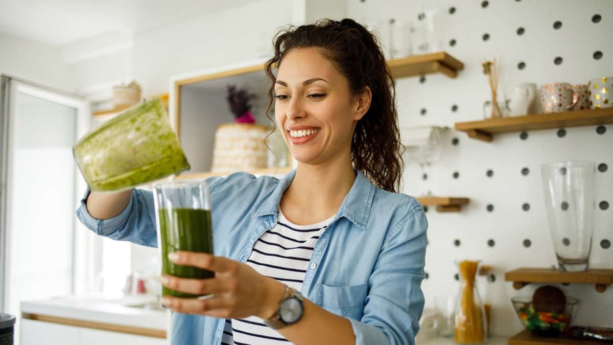 woman making and  drinking green smoothie kitchen home