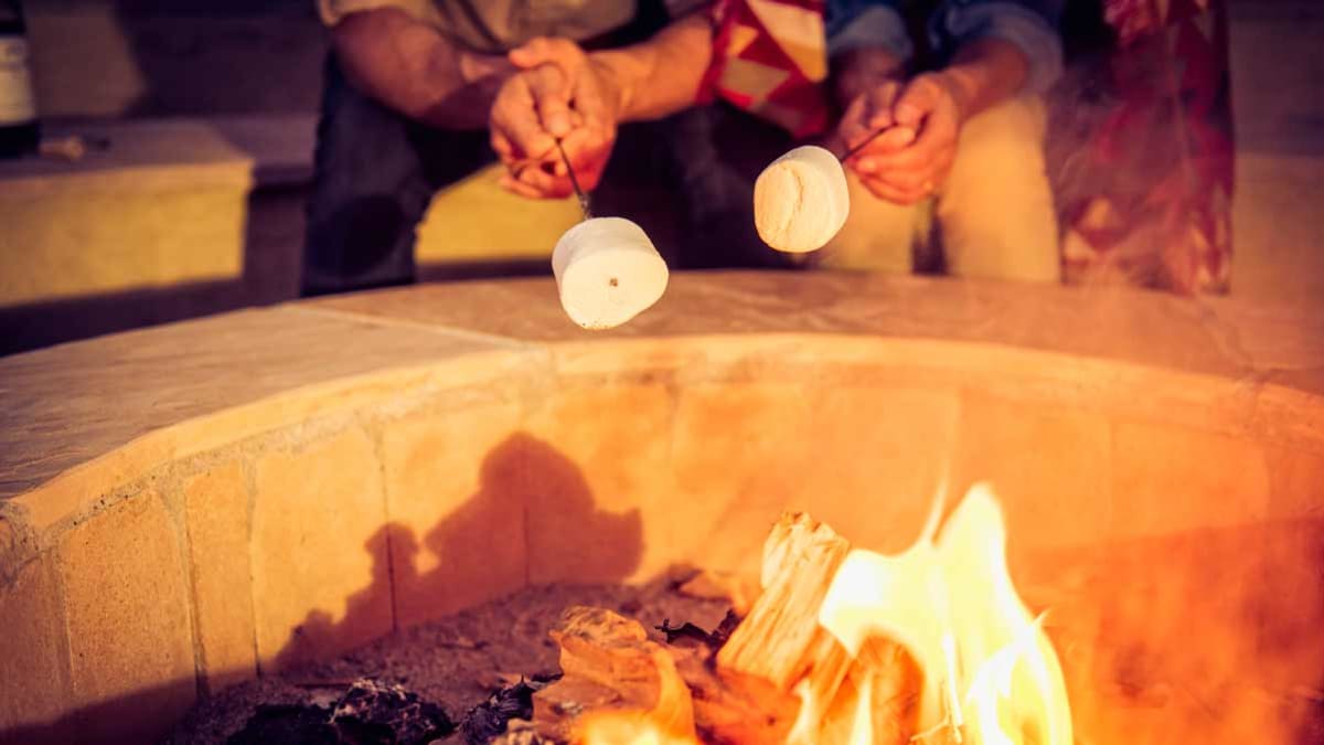 2 people roasting marshmallows at backyard fire pit