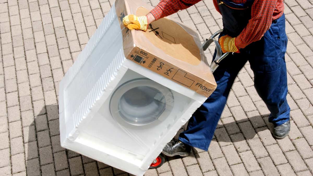 person moving packaged washer with handcart on brick path
