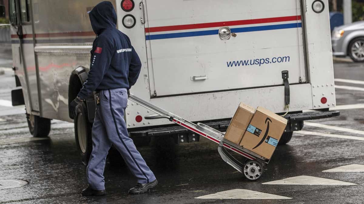 A U.S. Postal Service (USPS) worker delivers Amazon boxes in New York, U.S., on Tuesday, Oct. 13, 2020. Amazon.com Inc.'s two-day Prime Day sale kicks off on Tuesday and is expected to give the world's largest e-commerce company an early advantage over brick-and-mortar rivals still contending with pandemic-spooked consumers wary of battling Black Friday crowds.