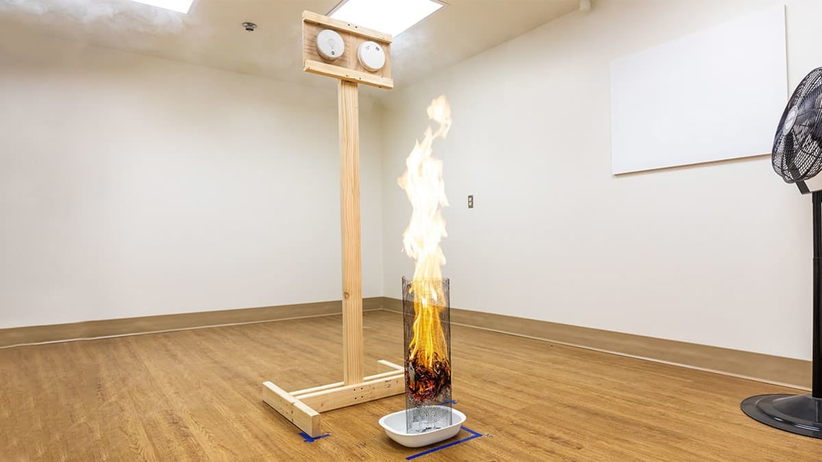A burning wad of paper sits in front of a pair of smoke detectors in an empty testing room to see how quickly the smoke detectors’ alarms will ring.