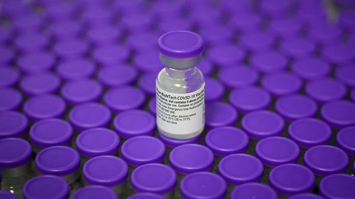 Surface filled with Vials of the Pfizer/BioNTech Covid-19 vaccine with purple tops, one vial stacked on top