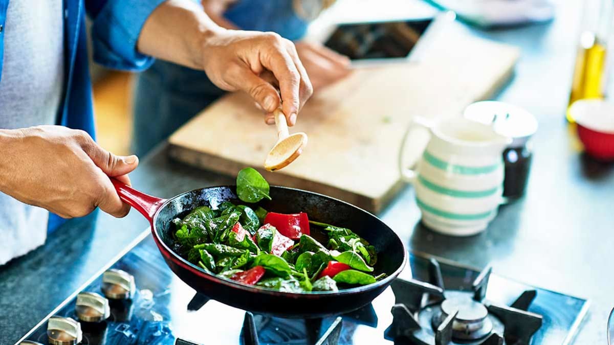 close up of person sautéing spinach and red peppers in cast iron skillet